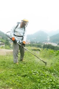 Man mowing grass with safety gear in a green hillside landscape in Rize, Turkey.